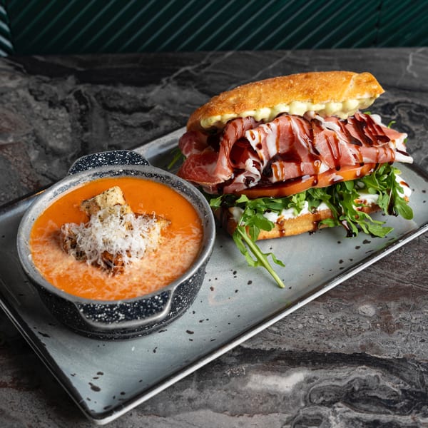 SNDWCH prosciutto sandwich with arugula, tomato, and balsamic glaze, served with tomato soup.