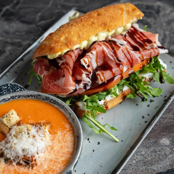 SNDWCH prosciutto sandwich with arugula and balsamic glaze, served with a side of tomato soup.
