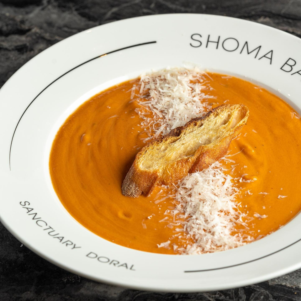 Orange tomato soup with a slice of toasted bread and grated cheese in a white bowl.