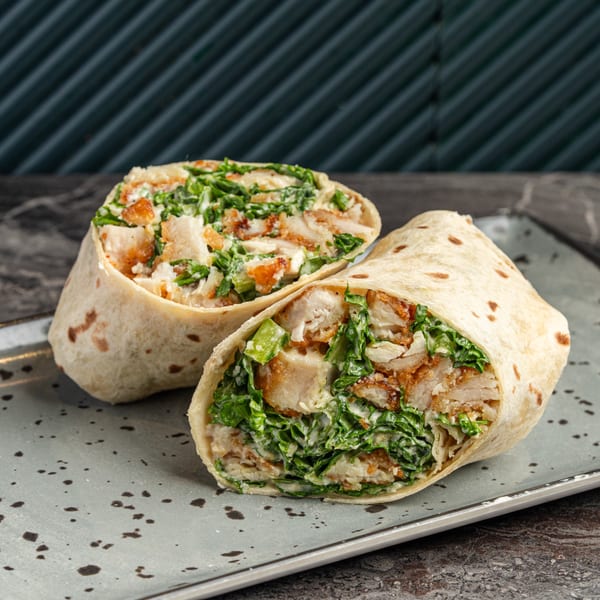 Two chicken Caesar wraps, filled with crispy chicken, lettuce, and creamy dressing, on a speckled gray plate.